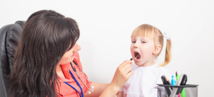 A pediatrician examining a young girl's mouth.