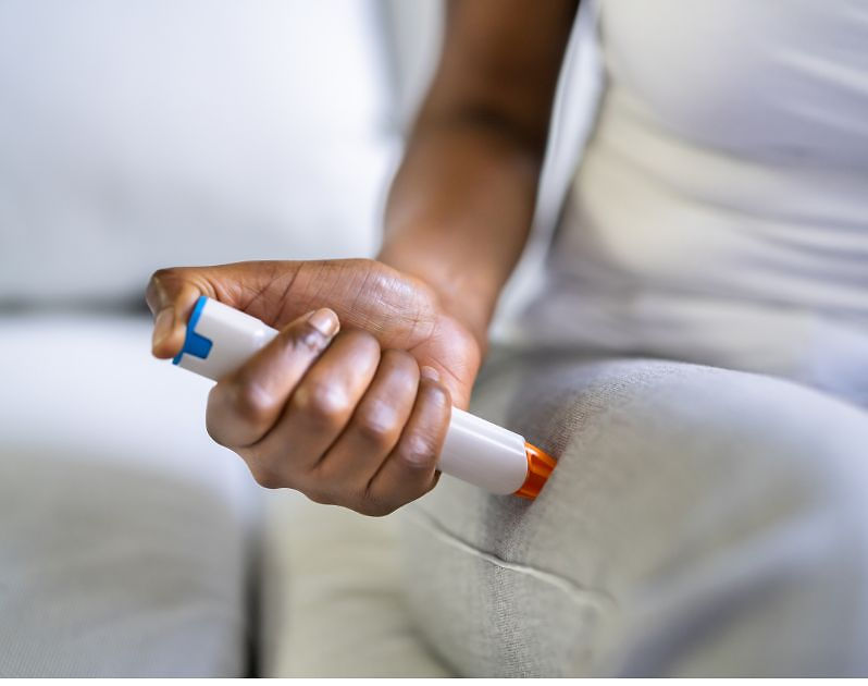 Woman self-administering an auto epinephrine injector on her thigh.